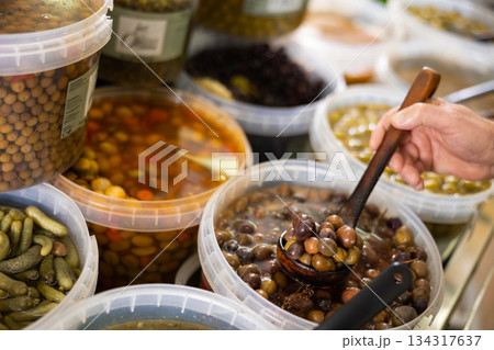 Supermarket or vegetable store, varieties of pickled olives with spices and customers hands 134317637