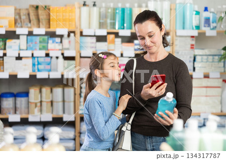 Woman with daughter in pharmacy scans QR code on mouthwash Woman with daughter in pharmacy scans QR code on mouthwash 134317787