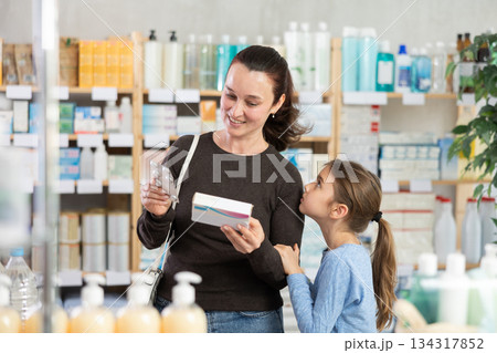 Woman with schoolgirl daughter are busy choosing tablet box at pharmacy Woman with schoolgirl daughter are busy choosing tablet box at pharmacy 134317852