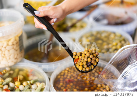 Supermarket or vegetable store, varieties of pickled olives with spices and customers hands 134317978