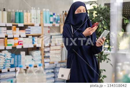 Young Muslim woman scanning QR-code on cream in drugstore Young Muslim woman scanning QR-code on cream in drugstore 134318042