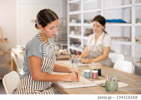 Girl kneads piece of raw clay with her hands, removes excess parts of material 134318168