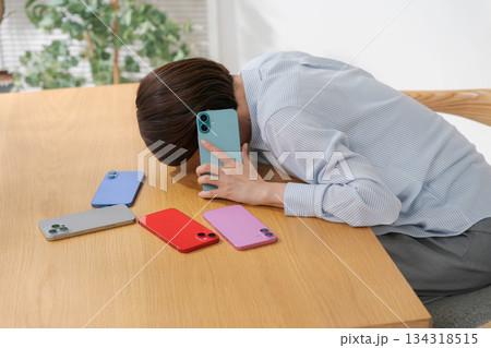 たくさんのスマホに囲まれて落ち込む女性 134318515
