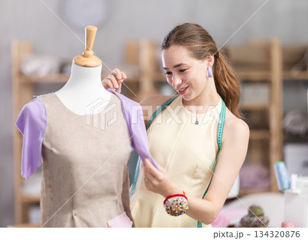 Female tailor sews new dress on a mannequin in sewing studio 134320876