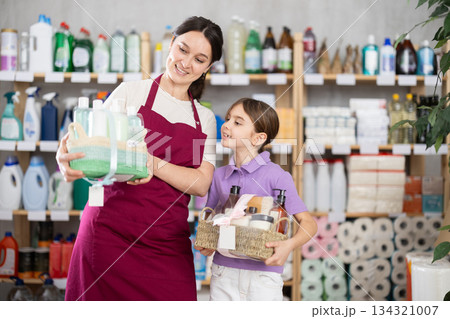 Friendly female salesperson helping little girl choose gift in goods store 134321007