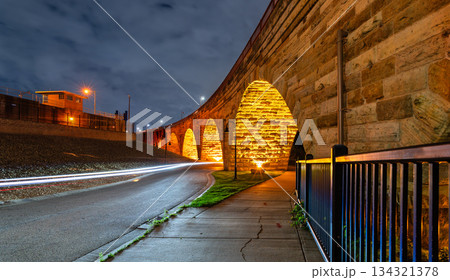 Stone Arch Bridge features illuminated arches at night in Minneapolis. Long exposure captures light trails on West River Parkway under a cloudy sky 134321378