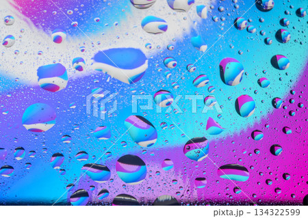 Abstract macro photography of water droplets on a vibrant neon blue and purple gradient background, creating a psychedelic liquid texture pattern. 134322599