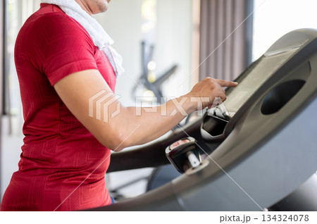 Close up of a man with towel on shoulder adjust speed while running exercising on treadmill in a gym Close up of a man with towel on shoulder adjust speed while running exercising on treadmill in a gym 134324078