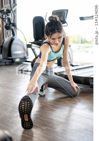 Pretty asian woman stretching arms and legs on floor warming up before exercising in fitness or gym. Pretty asian woman stretching arms and legs on floor warming up before exercising in fitness or gym. 134324096