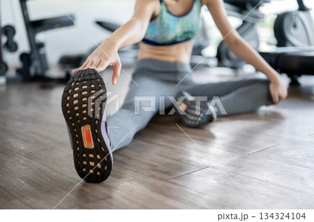 Close up of an athletic woman stretching arms and legs warming up before exercise in fitness or gym 134324104