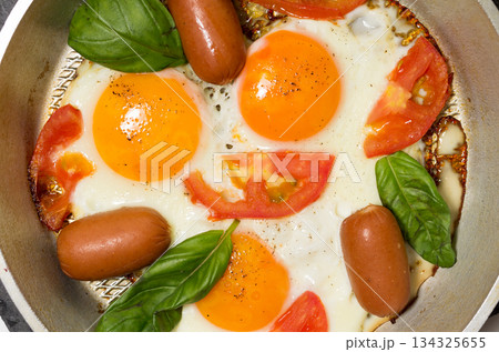 Fried eggs in the pan. Fried eggs with sausages and vegetables. 134325655