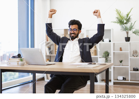 An Indian businessman is celebrating a success with his arms raised in the office 134325800