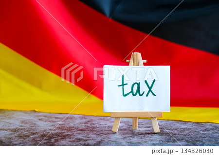 Paper note with words TAX on National symbol of Germany. German wave silky flag background. Tax planning system and economy policy  134326030