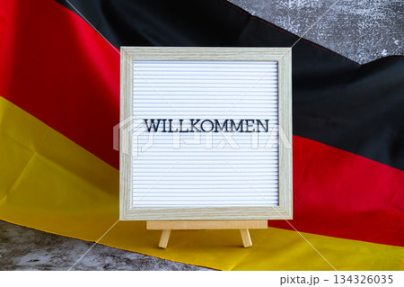 Letter board with message WILLKOMMEN Welcome National symbol of Germany. German wave silky flag background. Travel destination and tourism Letter board with message WILLKOMMEN Welcome National symbol of Germany. German wave silky flag background. Travel destination and tourism 134326035