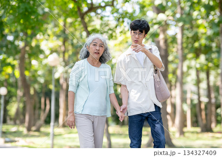 Young man grandson pointing as he holding hand and walking with old woman grandmother in garden park 134327409