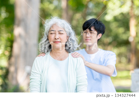 Glasses asian man caregiver nurse massaging shoulder old woman granny patient while sitting in park. Glasses asian man caregiver nurse massaging shoulder old woman granny patient while sitting in park. 134327444