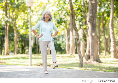 Old aged asian woman grandma with hands on waist lifting stretching leg while exercising in the park 134327458