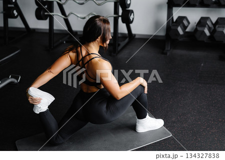 Woman is stretching body in gym. portrait and sport preparation. Young woman is stretching her leg in gym 134327838
