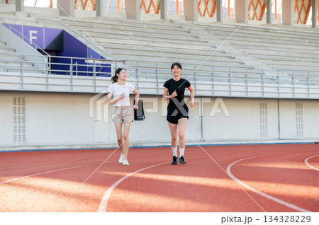 Full body asian woman friends running or jogging on racetrack exercising outdoors in sports stadium. Full body asian woman friends running or jogging on racetrack exercising outdoors in sports stadium. 134328229