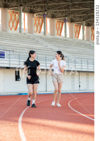 Asian woman friends running or jogging together on racetrack exercising outdoors in sports stadium 134328232