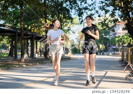 Pretty asian woman looking at friend while running or jogging on concrete road exercising in a park. 134328249