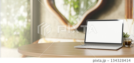 White screen laptop and coffee on wooden round table across door and window in a living room or cafe 134328414
