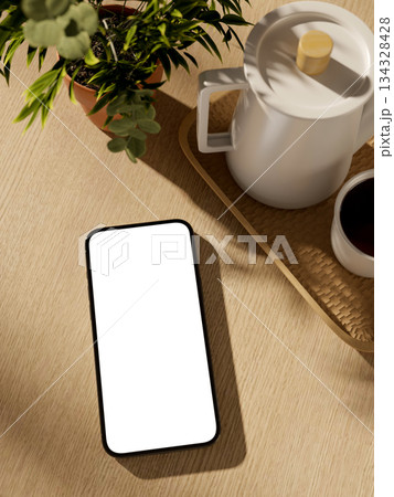 White screen smartphone with cup aside teapot and plant vase on wooden table in a living room or cafe. White screen smartphone with cup aside teapot and plant vase on wooden table in a living room or cafe. 134328428