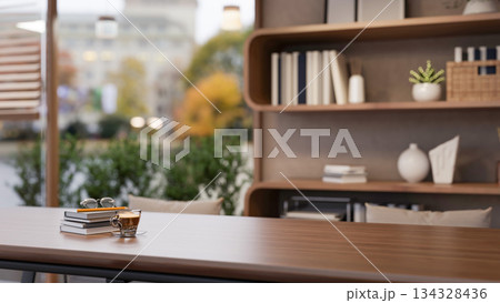 Coffee cup and eyeglasses on book on wooden table across display shelf and glass wall in living room Coffee cup and eyeglasses on book on wooden table across display shelf and glass wall in living room 134328436