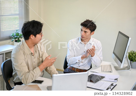 Asian businessman talking or discussing with a coworker aside computer at table in company's office. Asian businessman talking or discussing with a coworker aside computer at table in company's office. 134328902