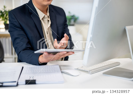Close up of businessman holding tablet and looking at computer on working table in company's office. 134328957