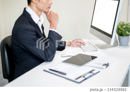 Close up businessman holding chin and thinking while looking at computer on table in company office. 134328982