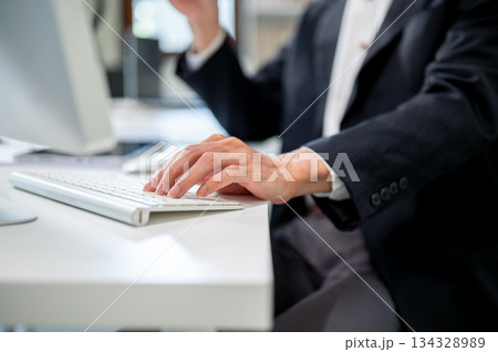 Close up of businessman's hand typing or resting on computer's keyboard at working table in office. 134328989