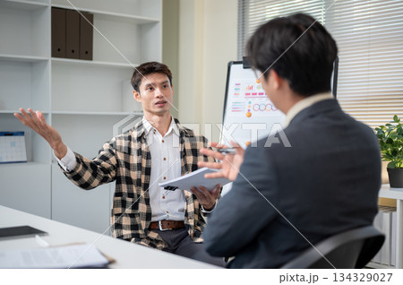 Asian man talking or discussing with a businessman boss after work presentation in company's office. Asian man talking or discussing with a businessman boss after work presentation in company's office. 134329027