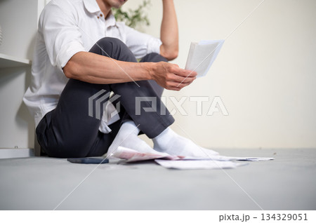Close up of an office worker man looking at bills and thinking while sitting on living room floor Close up of an office worker man looking at bills and thinking while sitting on living room floor 134329051