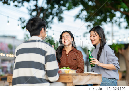 Asian woman holding bottle and friends eating fruit while sitting at table in campground restaurant. 134329392