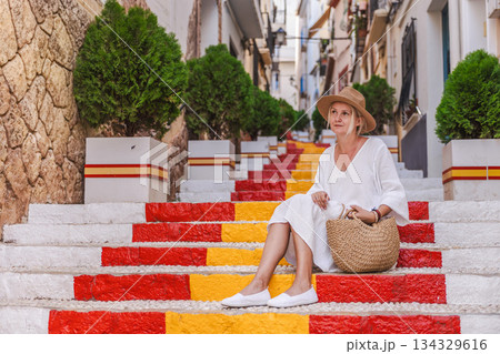 Young woman in a white dress sitting on the colourful Spanish Steps in the old town of Calpe, Spain, located in the historic Arrabal district Young woman in a white dress sitting on the colourful Spanish Steps in the old town of Calpe, Spain, located in the historic Arrabal district 134329616