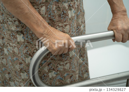 Asian elderly woman patient use toilet support rail in bathroom. 134329827