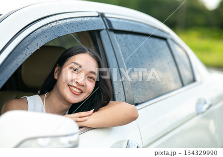 Pretty asian woman looking out from wet car window while travel going on road trip by driving a car 134329990