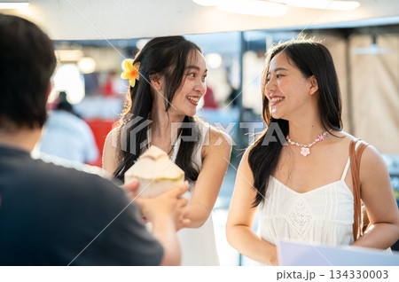 Pretty asian woman buying fresh coconut water while walking or shopping with friend in local market Pretty asian woman buying fresh coconut water while walking or shopping with friend in local market 134330003