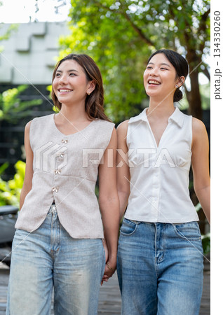 Pretty asian woman friends holding hands while standing or walking outdoors in cafe's garden or park 134330260