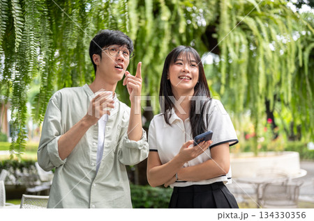 Pretty asian woman holding phone and glasses man holding coffee standing under tree in cafe's garden Pretty asian woman holding phone and glasses man holding coffee standing under tree in cafe's garden 134330356