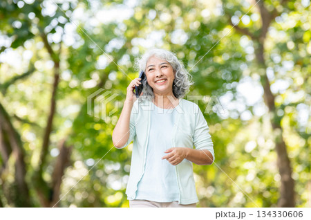 Old asian woman grandmother smiling and talking on smartphone while strolling or walking in park Old asian woman grandmother smiling and talking on smartphone while strolling or walking in park 134330606