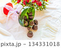 Chocolates are poured out of a green glass glass onto a white cloth with festive decor in the background.  134331018