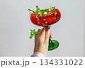Female hand holding red and green glass with glowing Christmas lights. Festive minimal composition with copy space for holiday, party or celebration concepts. 134331022