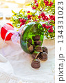 Chocolates are poured out of a green glass glass onto a white cloth with festive decor in the background. 134331023