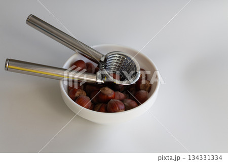 Stainless steel nutcracker in a plate with hazelnuts Stainless steel nutcracker in a plate with hazelnuts 134331334