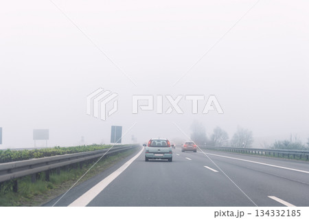 Driver POV of grey foggy misty rainy highway intercity road with low poor visibility on cold spring autumn morning. Seasonal bad rainy weather accident danger warning. car fog light 134332185