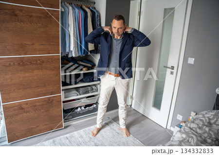 Man putting on a blue jacket in front of an open wardrobe. Getting dressed and preparing for the day. Man putting on a blue jacket in front of an open wardrobe. Getting dressed and preparing for the day. 134332833