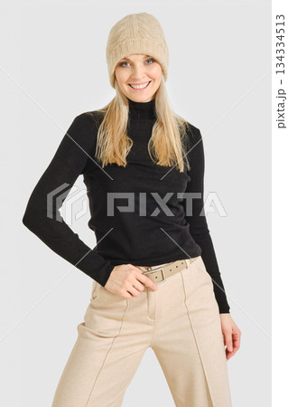 Woman wearing a black top and beige pants poses with a smile in a studio setting Woman wearing a black top and beige pants poses with a smile in a studio setting 134334513