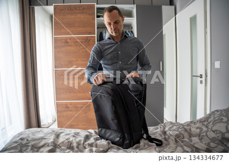 Man packing a black backpack on the bed. Preparing bag for the day ahead. Man packing a black backpack on the bed. Preparing bag for the day ahead. 134334677